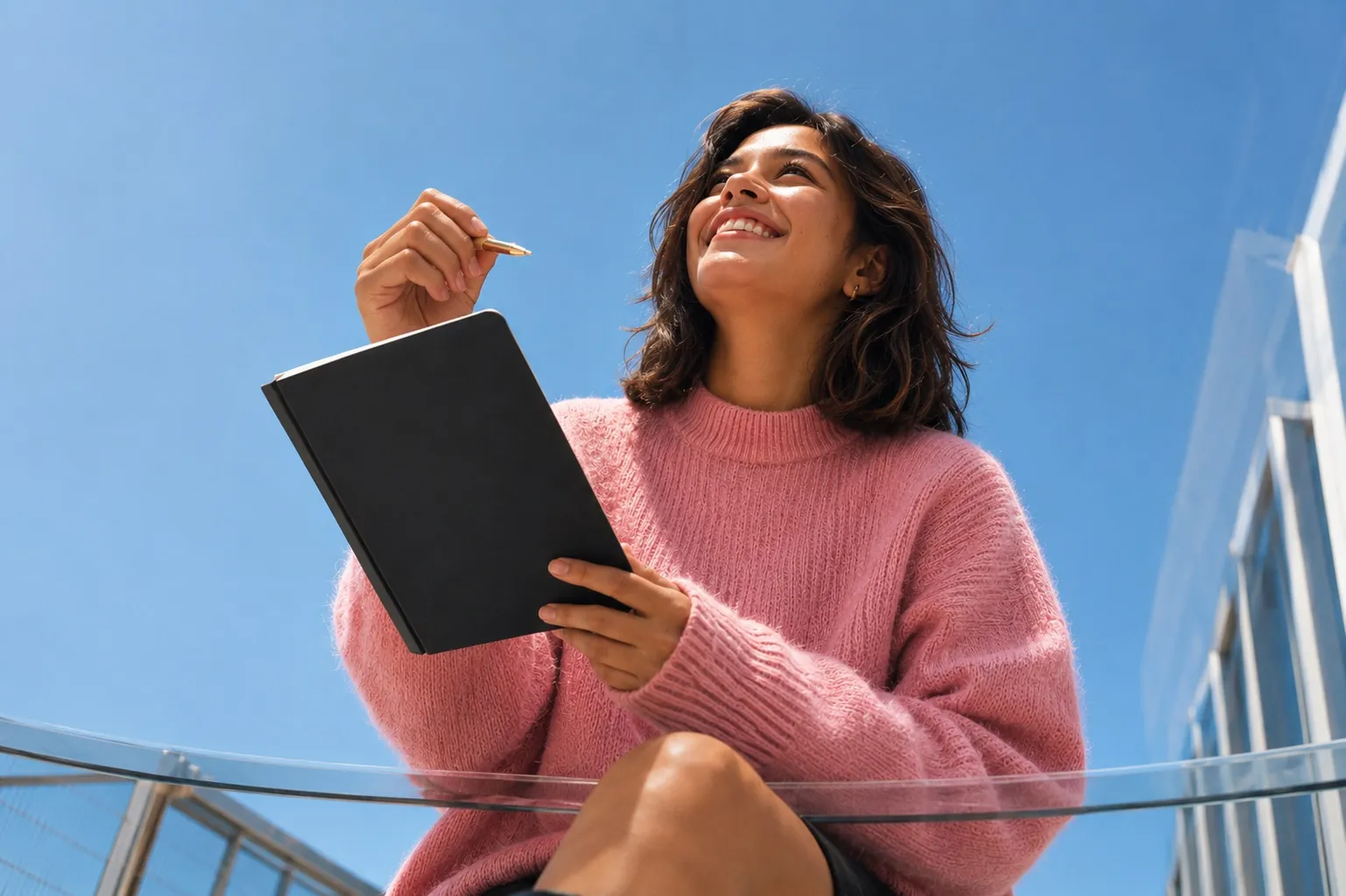 Woman in a pink sweater writing in a notebook outdoors